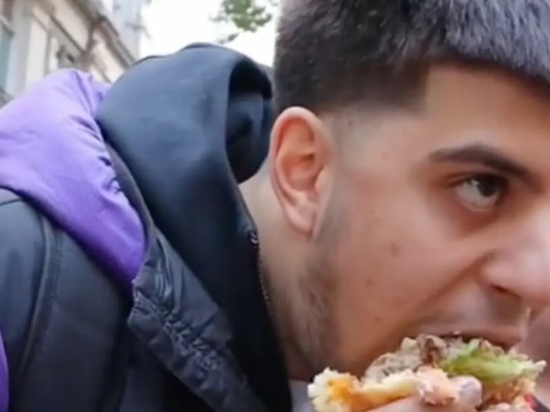 Un jeune homme mange un énorme burger devant une manifestation vegan